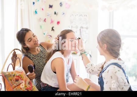 Three teenage girls doing make up and brushing hair in bedroom Stock Photo
