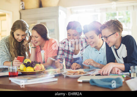 Group of teenagers using electronic devices at table in dining room Stock Photo