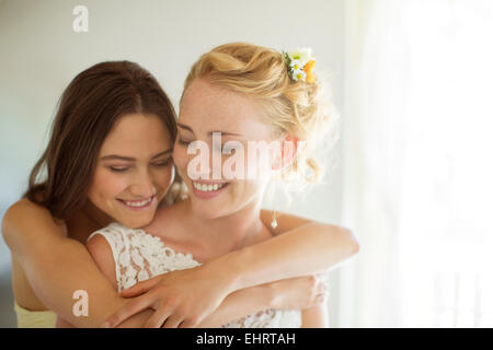 Bridesmaid embracing bride in bedroom Stock Photo