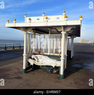 A Homeless man enjoys a cigarette while wrapped up in a sleeping bag from the cold in an Edwardian seafront shelter on Hove promenade in the City of Brighton and Hove, East Sussex Stock Photo