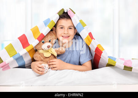 Playful kid holding a teddy bear under a blanket at home Stock Photo
