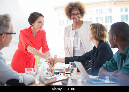 Office workers shaking hands at desk Stock Photo