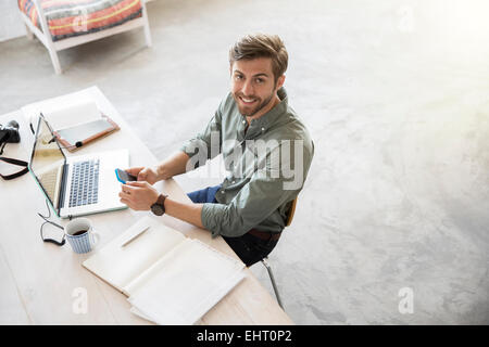 Portrait of young man sitting at desk with mobile phone and laptop Stock Photo