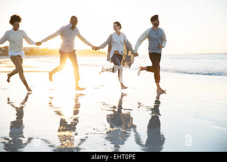Group of four friends holding hands and running on beach Stock Photo