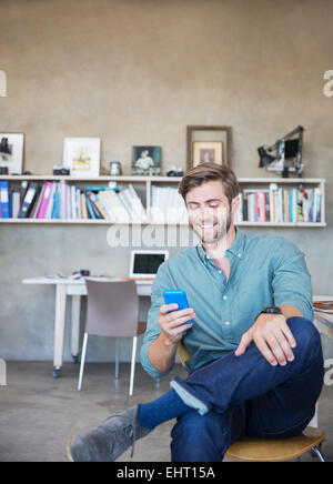 Young blonde man sitting with mobile phone in studio Stock Photo