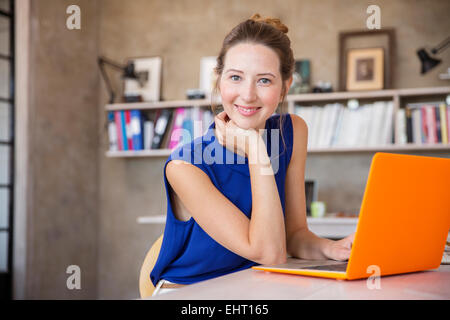 Portrait of young woman with orange laptop sitting in home office Stock Photo