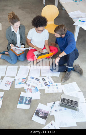 Three young people sitting on floor and working together in studio Stock Photo
