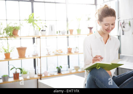 Woman sitting on kitchen counter and writing in her notebook Stock Photo
