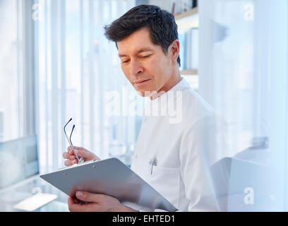 View of man in laboratory holding glasses and chart, looking away Stock Photo