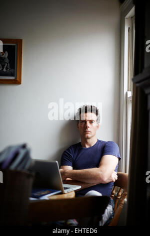 Man sitting at table with open laptop looking away Stock Photo