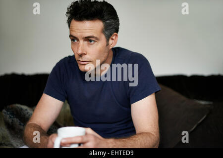 Man sitting on sofa holding mug looking sad Stock Photo