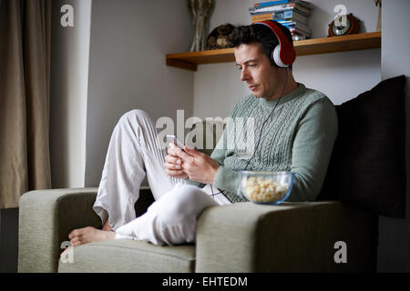 Man sitting in armchair with headphones using smartphone Stock Photo