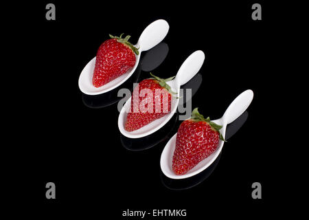 three strawberries in faience spoons placed on a glass plate Stock Photo