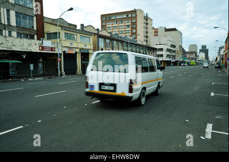White minibus taxi transporting commuters, travelling on Dr Yusuf Dadoo street past buildings of the Indian Quarter, city of Durban, South Africa Stock Photo