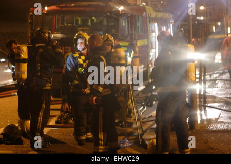 Ilford, London, UK. Wednesday 18th March 2015. 11 Rescued from fire in flats above a shop in Ilford. Six Fire engines from across east London tackled a fire in a block of flats in Ilford early this morning. London Fire Brigade reported that Six adults and five children including a baby were rescued by firefighters using ladders. It is reported that the fire broke out in a shop below the flats. Stock Photo