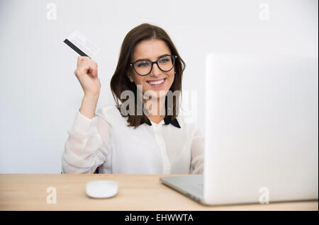 Happy businesswoman sitting at the table with laptop and holding bank card Stock Photo