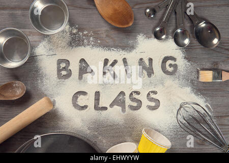 Word baking class written in white flour on a old wooden table from top view in vintage tone, surrounding by baking tools. Stock Photo