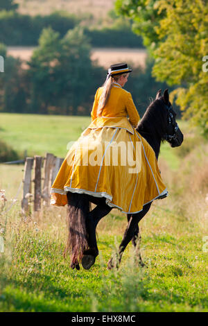 Friesian Horse Rider wearing baroque riding habit riding black Friesian Horse path summer Germany Stock Photo