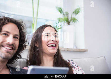 Couple laughing on couch with using digital tablet, Munich, Bavaria, Germany Stock Photo