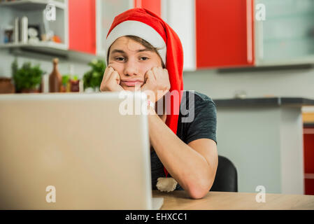 Bored young man with Santa hat using laptop, Munich, Bavaria, Germany Stock Photo