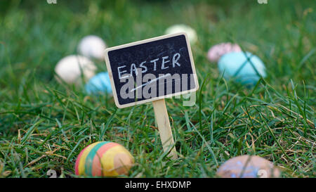 Easter written on a chalkboard standing in grass between easter eggs Stock Photo