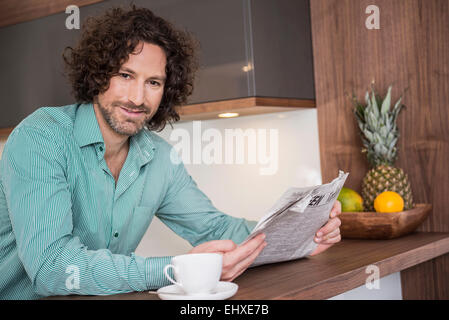 Man sitting in a kitchen and reading a newspaper, Munich, Bavaria, Germany Stock Photo