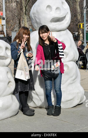 Two Asian women take a selfie near the marble snowmen by Peter Rigli in the Flatiron District of Manhattan, New York City Stock Photo