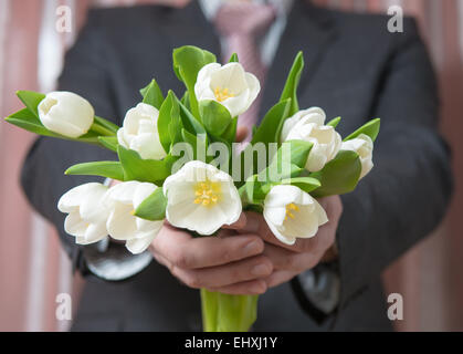 Man - businessman in a suit gives a bouquet of flowers, white tulips Stock Photo