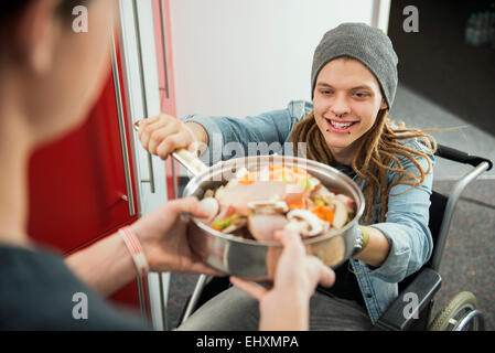 Young man in wheelchair handed a pan with a raw dish to a woman, Munich, Bavaria, Germany Stock Photo