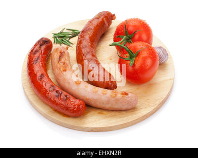 Various grilled sausages with condiments and tomatoes on cutting board. Isolated on white background Stock Photo