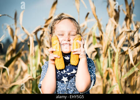 Girl holding corn on the cob in field
