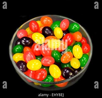 Fruit jelly beans in many colors in a glass bowl on a black background. Stock Photo