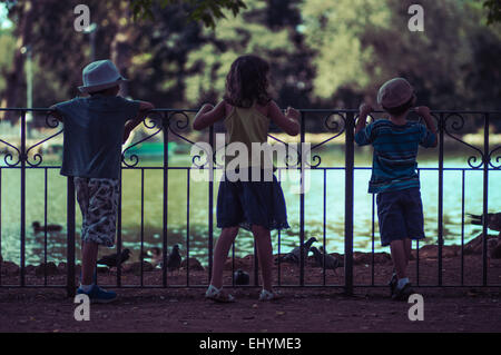 Three children looking at ducks on a lake, Italy Stock Photo