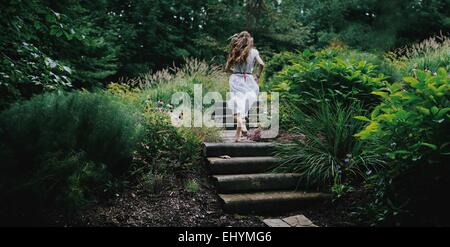 Rear view of young woman running up steps in a garden Stock Photo