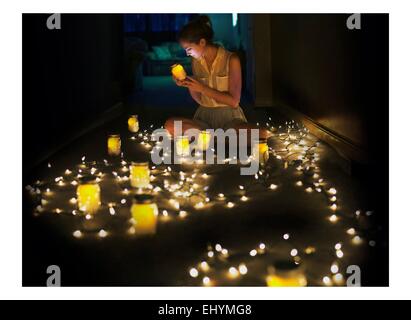 Young woman sitting on floor surrounded by fairy lights and tea lights Stock Photo