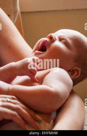 Baby yawning in his mother's arms Stock Photo