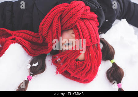 Girl with red scarf covering face lying in the snow Stock Photo