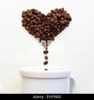 Coffee beans in shape of heart dropping into a coffee cup Stock Photo