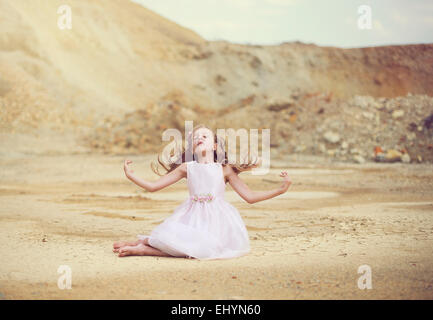 Girl sitting in the desert with her arms outstretched Stock Photo