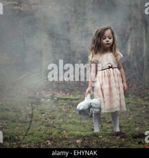 Girl standing in the woods holding a teddy bear Stock Photo