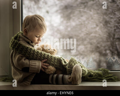 Boy sitting on a window sill with a teddy bear Boy sitting on a window sill with a teddy bear