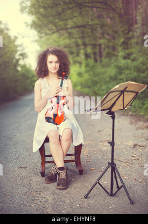 Portrait of a young woman sitting with her violin Stock Photo