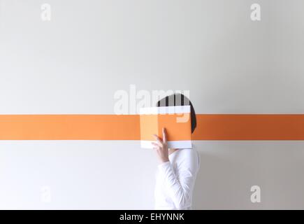 Side view of a woman hiding her face behind a book with an orange stripe Stock Photo