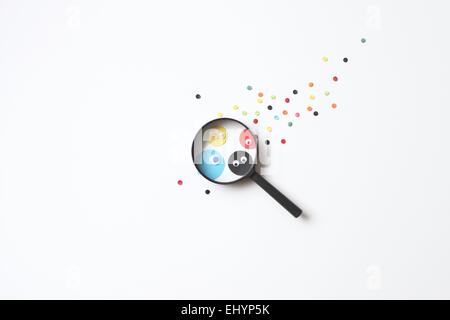 Paper dots with googly eyes seen through a magnifying glass Stock Photo