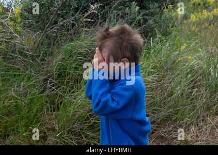 Child playing hide and seek in field, 4 year old boy Stock Photo