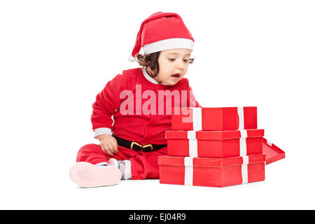 Curious baby girl sitting on the floor next to a pile of Christmas presents Stock Photo