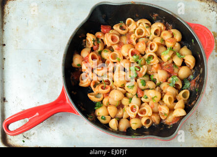 Gomiti elbow pasta shells in arrabbiata tomato, garlic and chili sauce, garnished with chopped parsley, cooking in a frying pan. Stock Photo