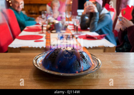 Horizontal view of a Christmas pudding alight during a family Christmas lunch. Stock Photo