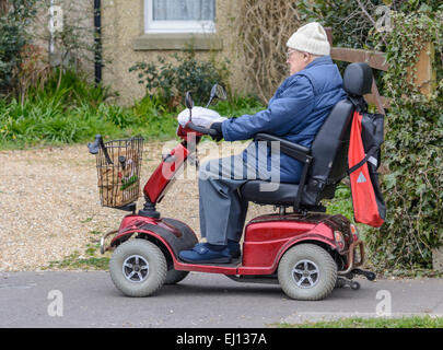 Mobility scooter - Electric mobility scooter being ridden by an elderly man along a pavement. Stock Photo