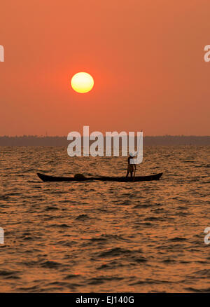 A fishing boat in silhouette at sunset on the Vembanad Lake in Kumarakom, Kerala India Stock Photo
